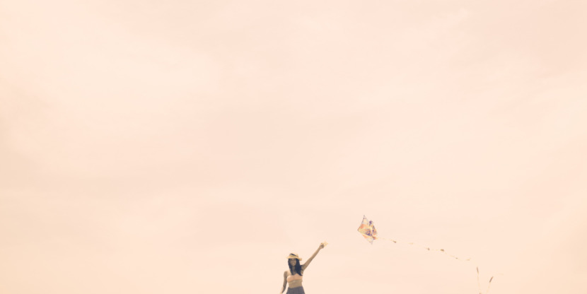 Young woman flying kite on summery day at the beach